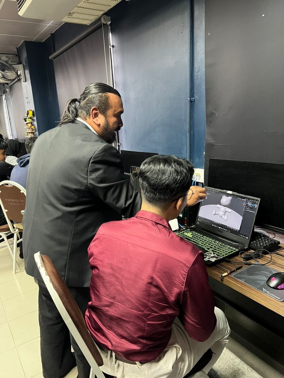 Norzaful pointing at a student's laptop showing a character sculpt in Blender